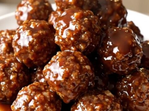 A close-up of glossy, barbecue-glazed beef meatballs topped with bacon bits in a slow cooker.