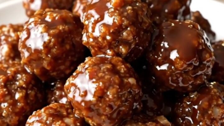 A close-up of glossy, barbecue-glazed beef meatballs topped with bacon bits in a slow cooker.