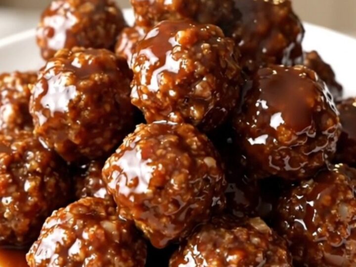 A close-up of glossy, barbecue-glazed beef meatballs topped with bacon bits in a slow cooker.