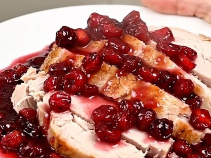 A sliced turkey breast topped with a glossy cranberry apple sauce on a white plate.