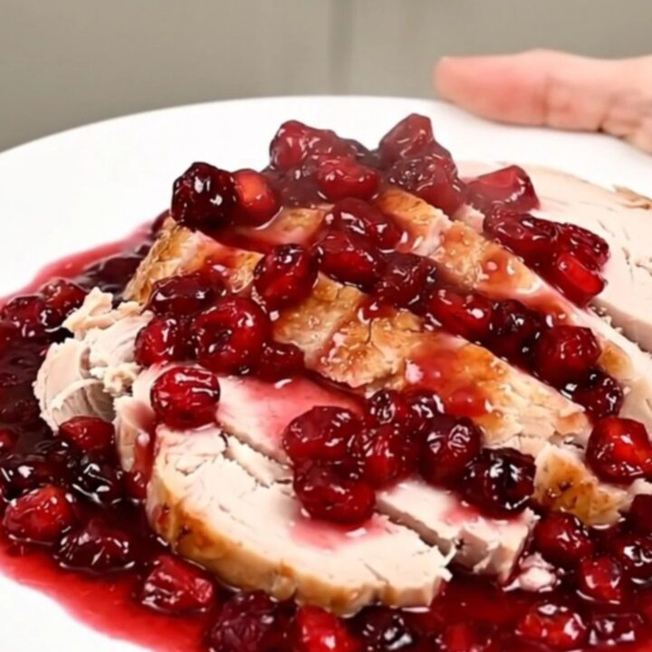A sliced turkey breast topped with a glossy cranberry apple sauce on a white plate.