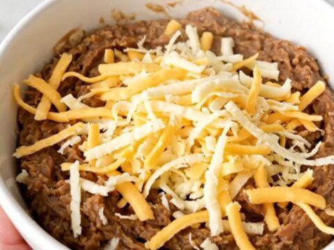 A top-down view of a black slow cooker filled with a creamy, cheesy refried bean dip ready to be served.