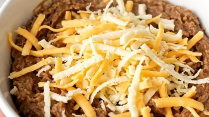 A top-down view of a black slow cooker filled with a creamy, cheesy refried bean dip ready to be served.