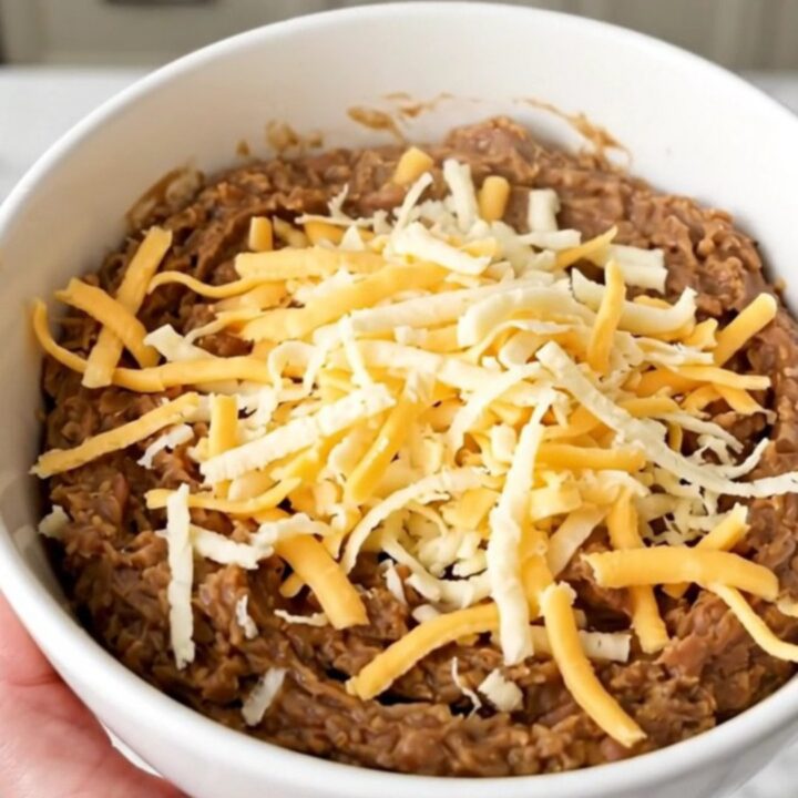 A top-down view of a black slow cooker filled with a creamy, cheesy refried bean dip ready to be served.