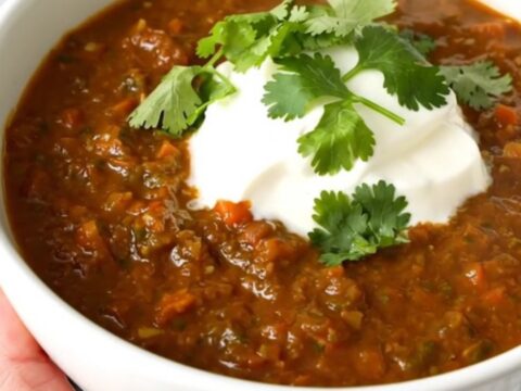 A steaming bowl of salsa verde beef chili garnished with fresh cilantro and a dollop of sour cream.