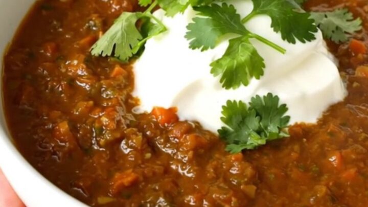 A steaming bowl of salsa verde beef chili garnished with fresh cilantro and a dollop of sour cream.