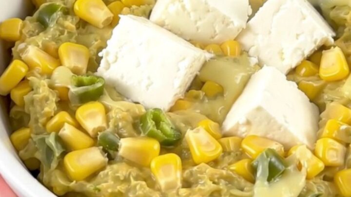 A close-up of a creamy corn and green chile dip in a white bowl with steam rising.