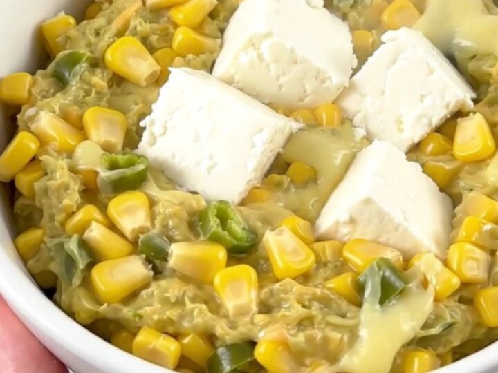 A close-up of a creamy corn and green chile dip in a white bowl with steam rising.