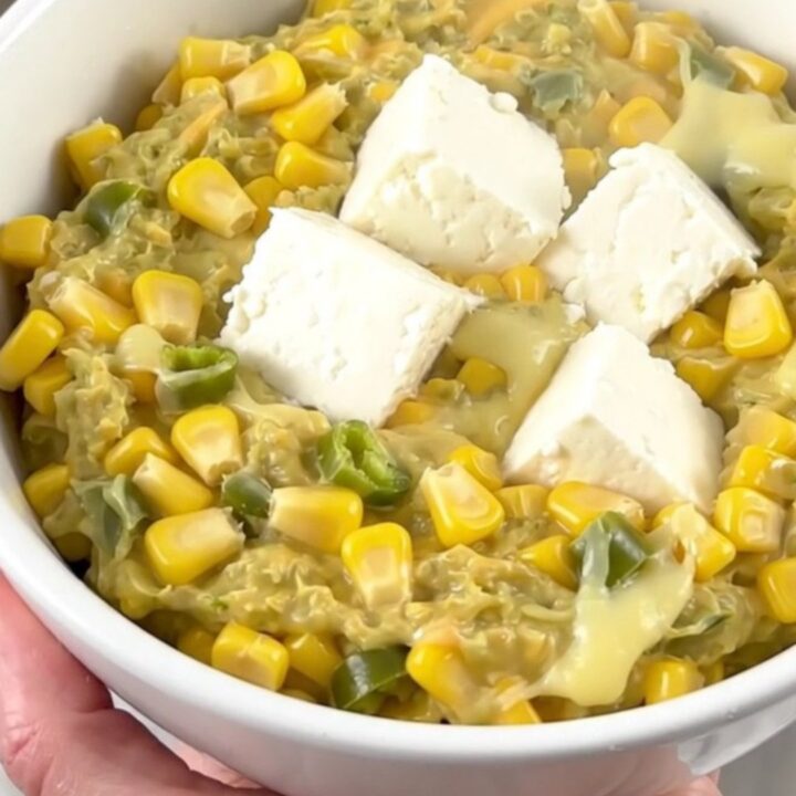 A close-up of a creamy corn and green chile dip in a white bowl with steam rising.