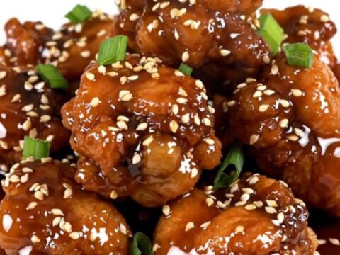 A close-up of glossy sesame chicken in a slow cooker, showing tender pieces coated in a rich, dark honey soy glaze.