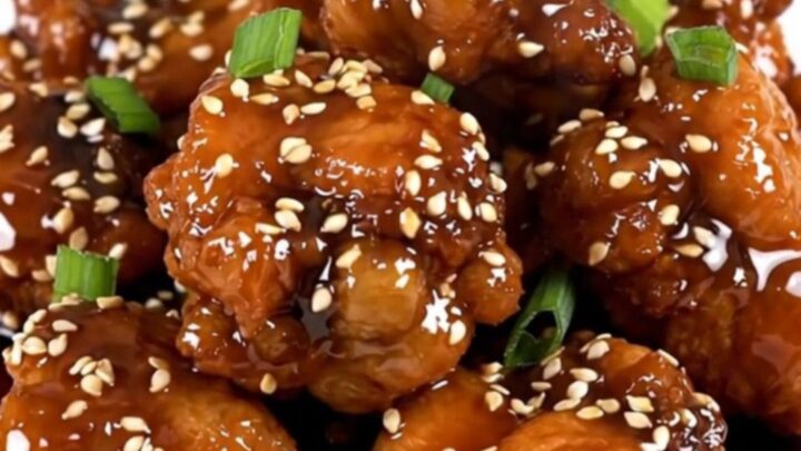 A close-up of glossy sesame chicken in a slow cooker, showing tender pieces coated in a rich, dark honey soy glaze.