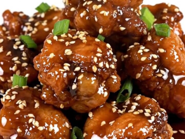 A close-up of glossy sesame chicken in a slow cooker, showing tender pieces coated in a rich, dark honey soy glaze.
