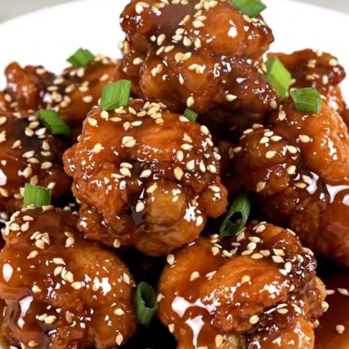 A close-up of glossy sesame chicken in a slow cooker, showing tender pieces coated in a rich, dark honey soy glaze.