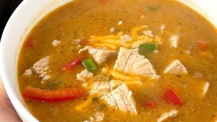 A steaming bowl of creamy chicken fajita soup garnished with fresh cilantro on a white countertop.