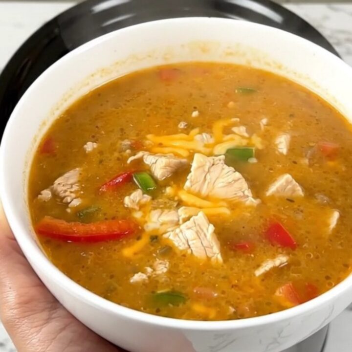 A steaming bowl of creamy chicken fajita soup garnished with fresh cilantro on a white countertop.