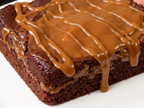 A warm, steaming chocolate turtle dump cake served on a white plate with visible pecans and caramel sauce.