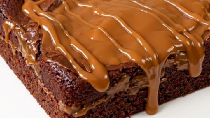 A warm, steaming chocolate turtle dump cake served on a white plate with visible pecans and caramel sauce.