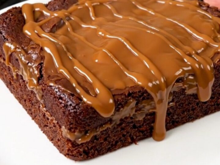 A warm, steaming chocolate turtle dump cake served on a white plate with visible pecans and caramel sauce.