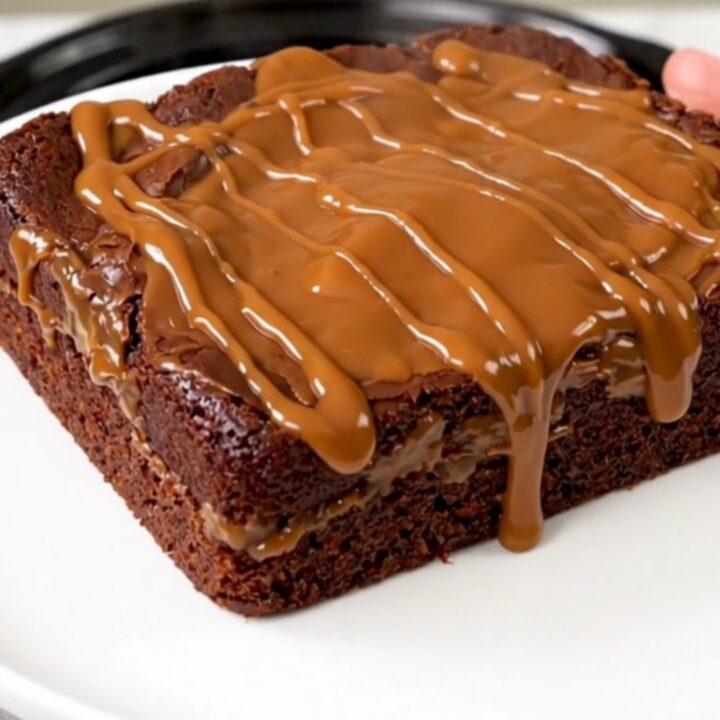 A warm, steaming chocolate turtle dump cake served on a white plate with visible pecans and caramel sauce.