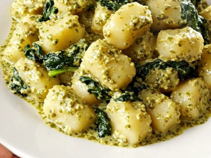 A plate of creamy pesto gnocchi with spinach in a white dish on a kitchen counter.