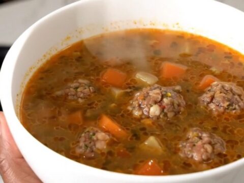 A steaming bowl of Mexican Albondigas soup featuring meatballs, carrots, and zucchini in a clear, savory broth.