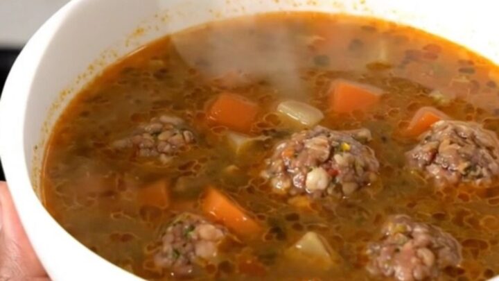 A steaming bowl of Mexican Albondigas soup featuring meatballs, carrots, and zucchini in a clear, savory broth.