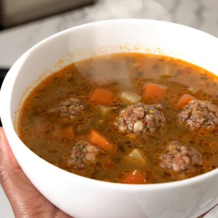 A steaming bowl of Mexican Albondigas soup featuring meatballs, carrots, and zucchini in a clear, savory broth.