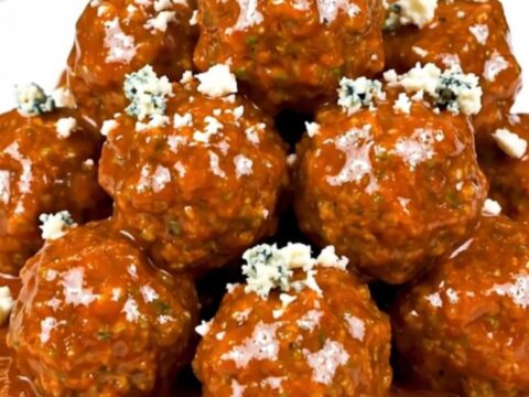 Slow cooker filled with saucy buffalo beef meatballs garnished with crumbled blue cheese.