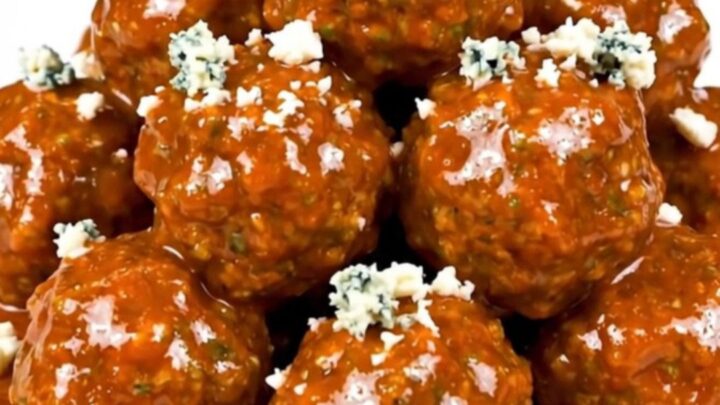 Slow cooker filled with saucy buffalo beef meatballs garnished with crumbled blue cheese.