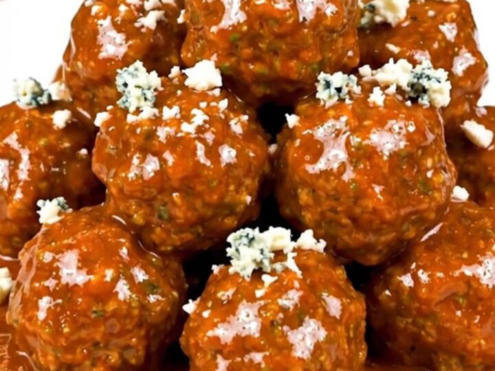 Slow cooker filled with saucy buffalo beef meatballs garnished with crumbled blue cheese.