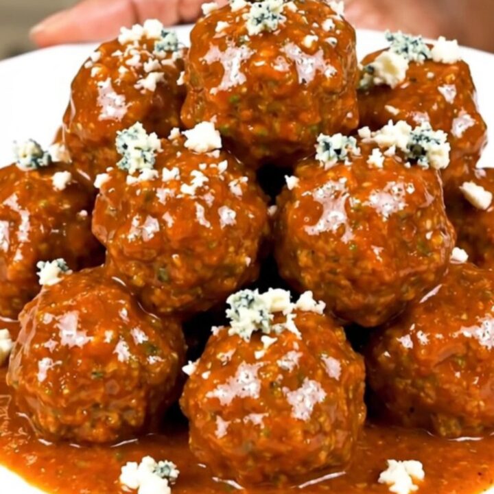 Slow cooker filled with saucy buffalo beef meatballs garnished with crumbled blue cheese.