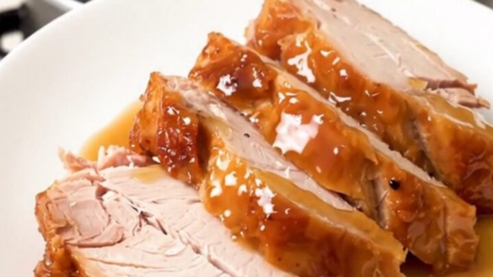 A close-up of sliced, glossy, fully cooked honey soy turkey breast on a white plate.