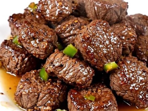 A close-up of glossy, slow-cooked Cajun steak bites with green bell peppers on a white plate.
