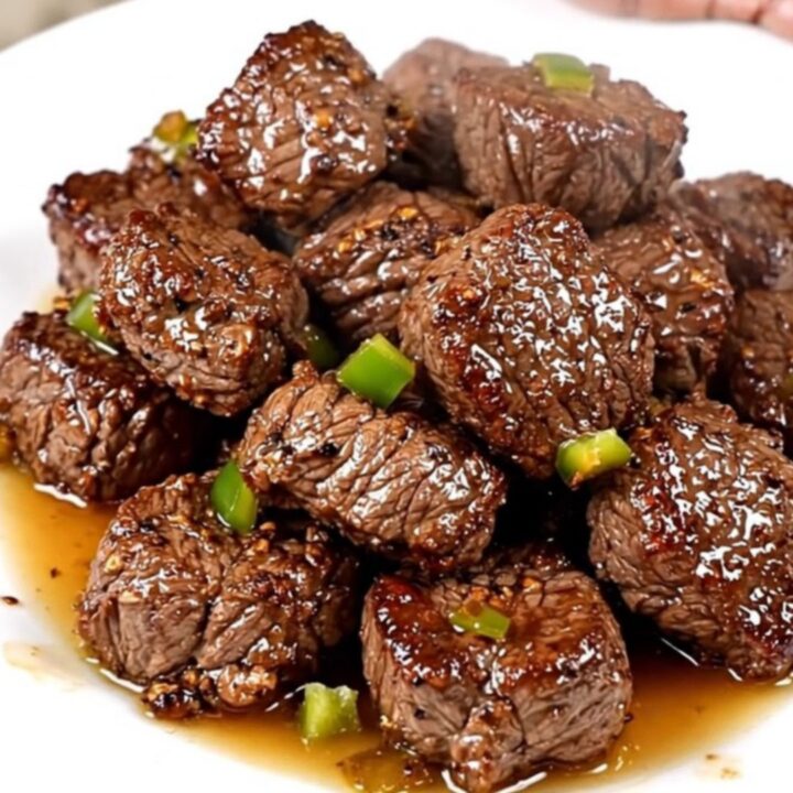 A close-up of glossy, slow-cooked Cajun steak bites with green bell peppers on a white plate.