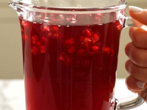 A warm glass mug filled with deep-red spiced pomegranate apple cider, garnished with a cinnamon stick.