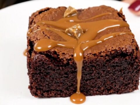 A top-down view of a black slow cooker filled with rich, glossy chocolate brownie batter topped with chocolate chunks