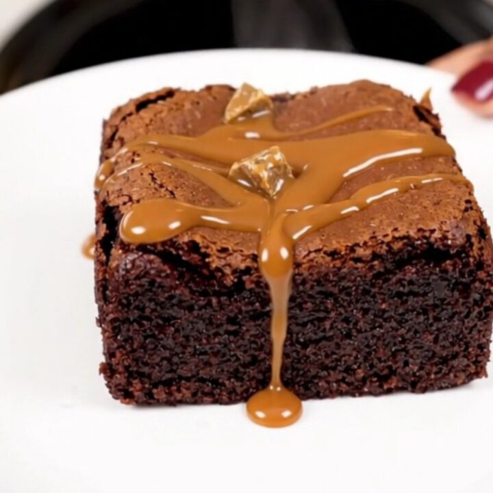 A top-down view of a black slow cooker filled with rich, glossy chocolate brownie batter topped with chocolate chunks