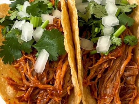 A plate of shredded pork birria tacos served on a white plate with fresh garnishes.