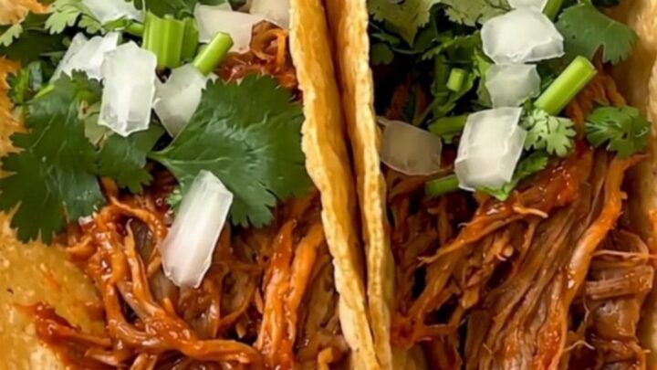 A plate of shredded pork birria tacos served on a white plate with fresh garnishes.