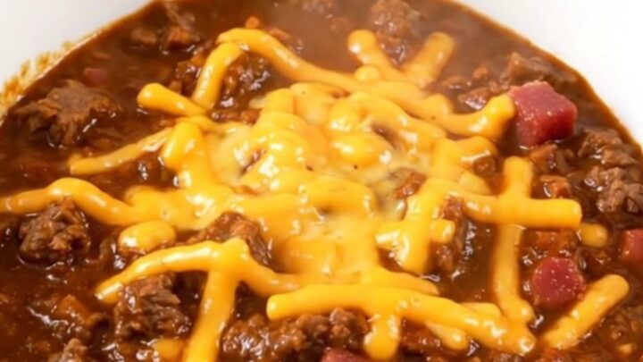 A steaming, glossy bowl of bacon cheeseburger chili topped with shredded cheddar cheese.