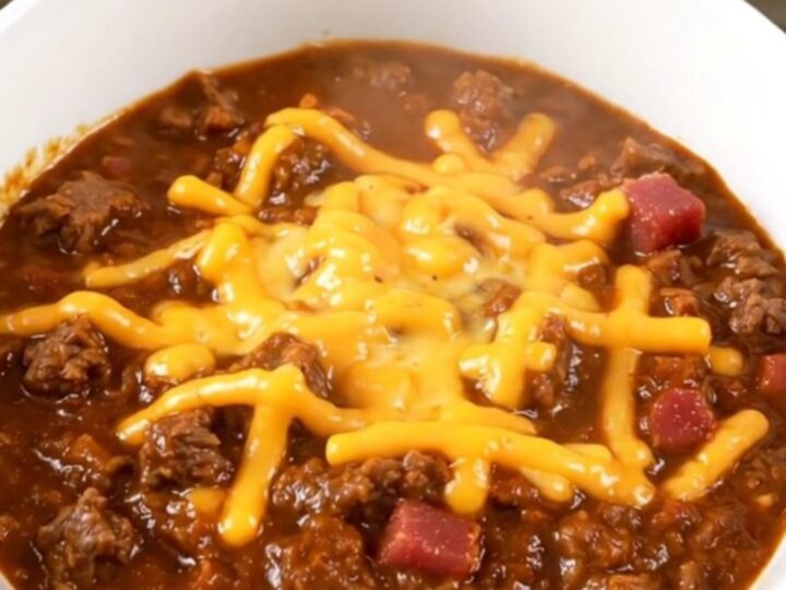 A steaming, glossy bowl of bacon cheeseburger chili topped with shredded cheddar cheese.