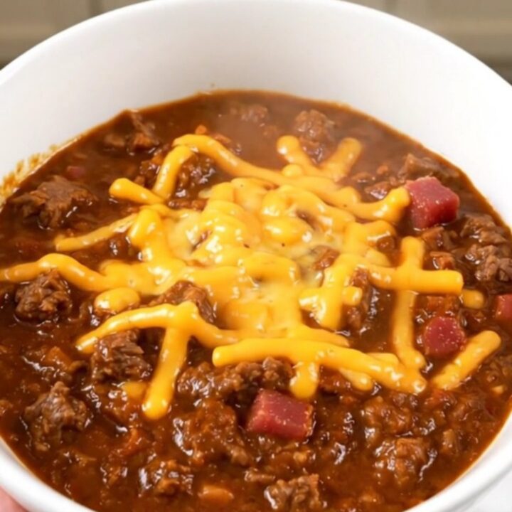 A steaming, glossy bowl of bacon cheeseburger chili topped with shredded cheddar cheese.