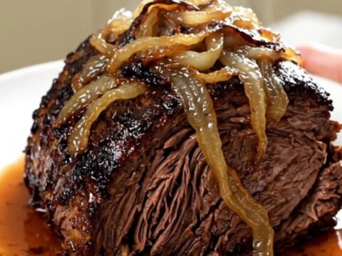 A tender, slow-cooked beef chuck roast topped with caramelized sweet onions and crispy bacon on a white plate.