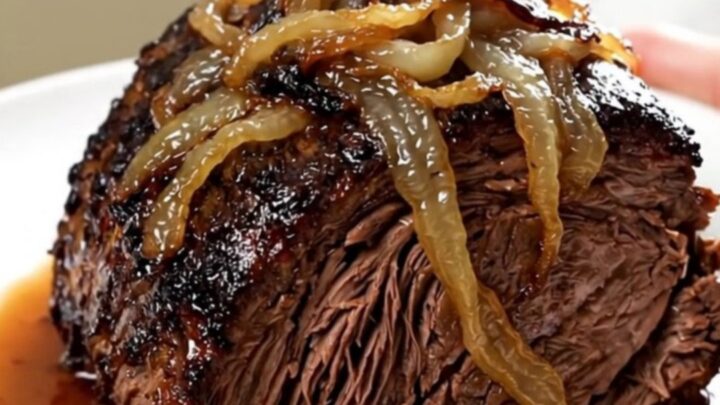 A tender, slow-cooked beef chuck roast topped with caramelized sweet onions and crispy bacon on a white plate.