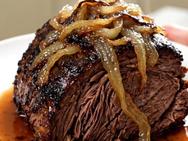 A tender, slow-cooked beef chuck roast topped with caramelized sweet onions and crispy bacon on a white plate.