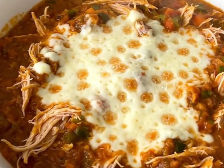 A close-up of a bowl filled with shredded chicken chili topped with melted mozzarella cheese.