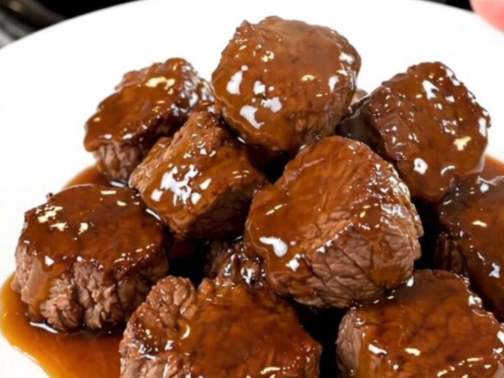 A close-up of glistening honey garlic steak bites served on a white plate, showing the rich glaze.