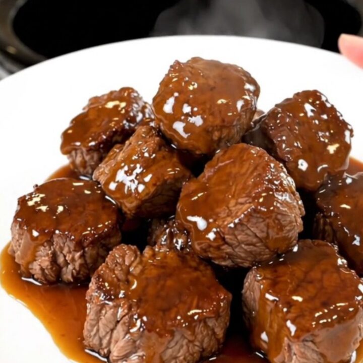 A close-up of glistening honey garlic steak bites served on a white plate, showing the rich glaze.