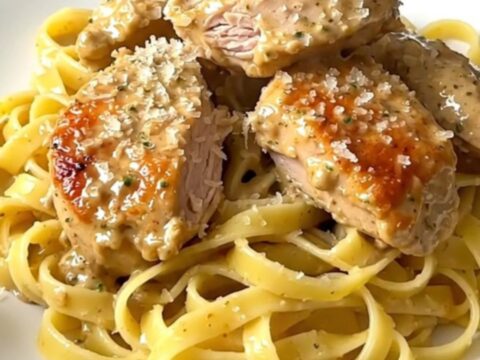Creamy lemon parmesan chicken served over pasta on a white plate.