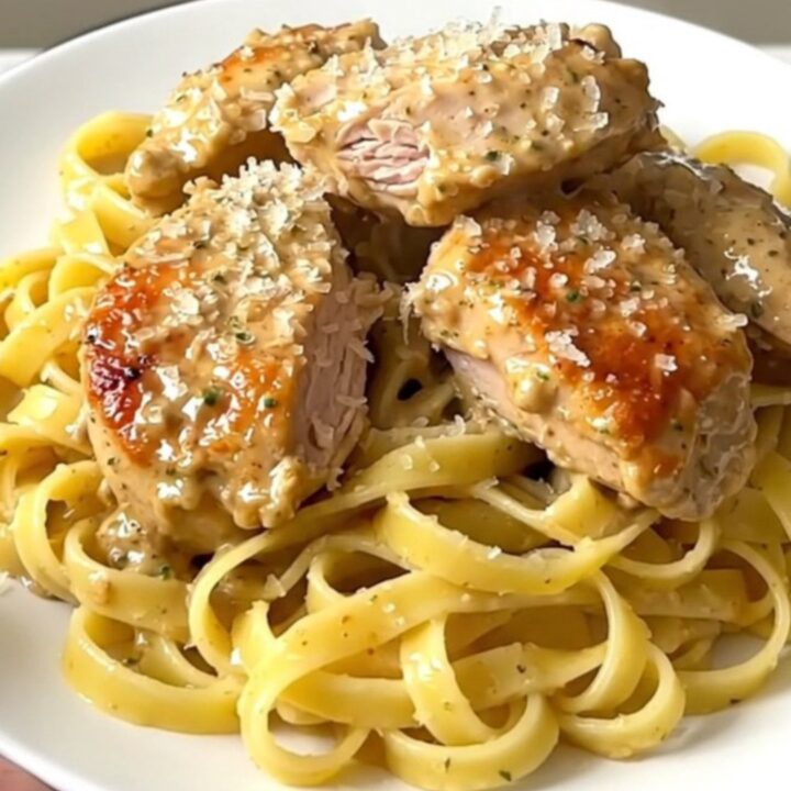 Creamy lemon parmesan chicken served over pasta on a white plate.
